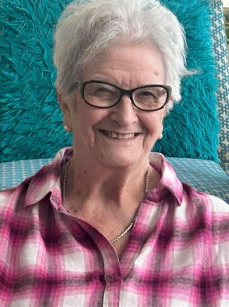 Picture of Sheila Dommett, with glasses, facing camera, smiling, wearing open-necked pink checked shirt